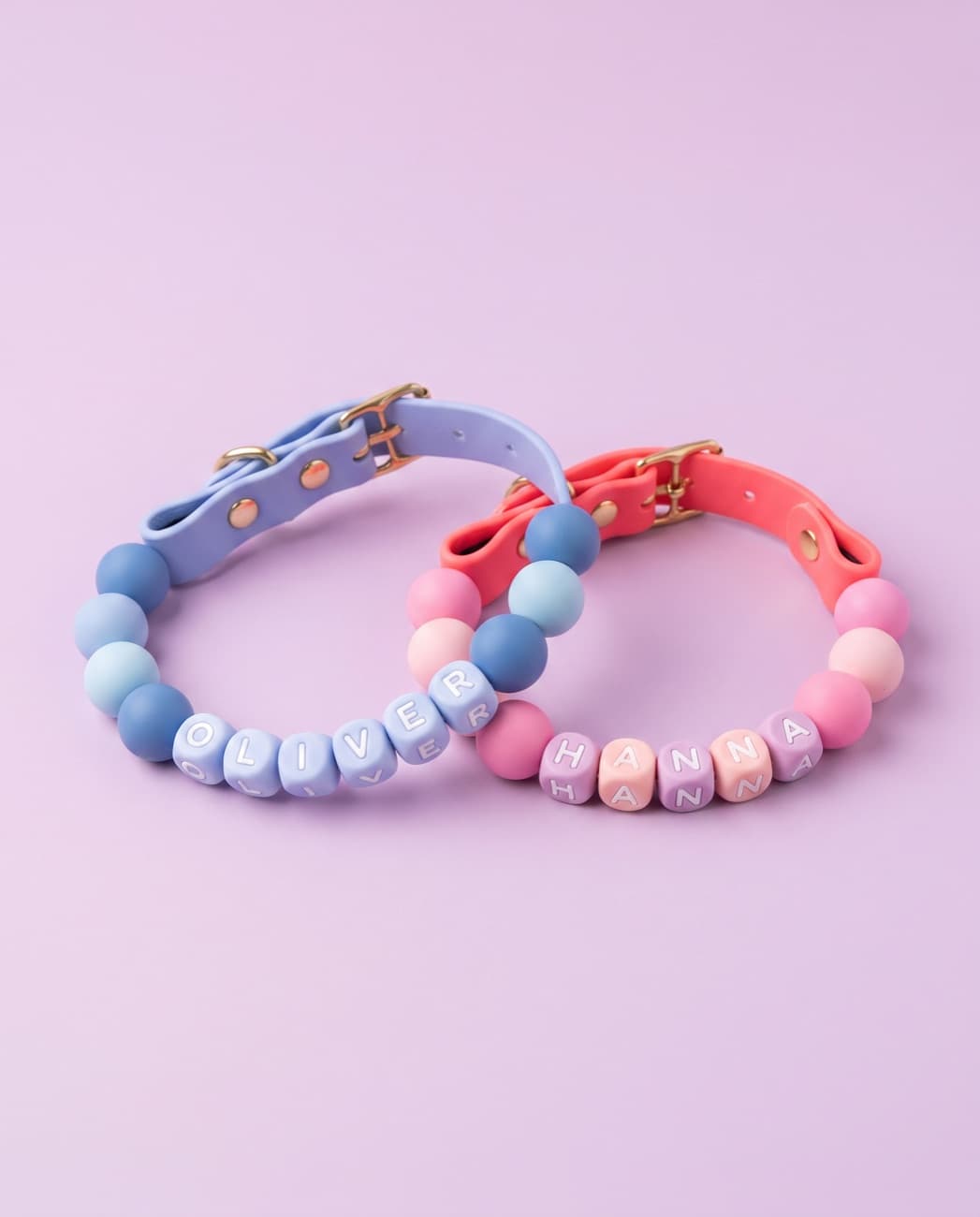 A blue collar and a pink collar resting together on a soft lilac background