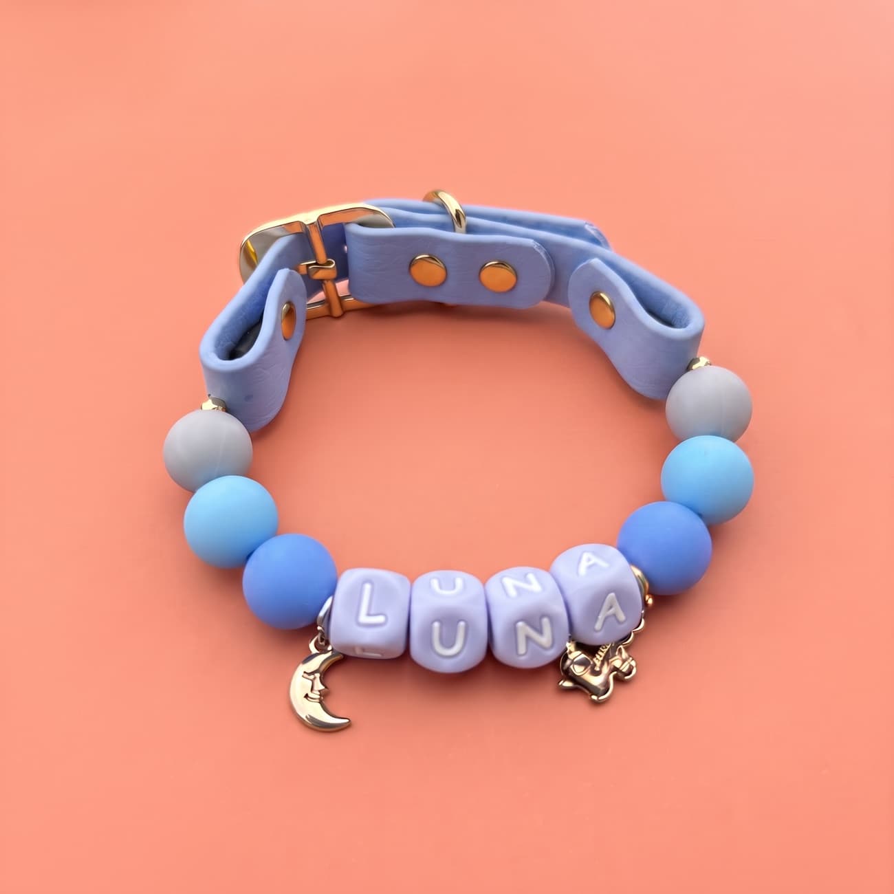 Periwinkle-blue beaded collar with moon and anchor charms on a warm coral background