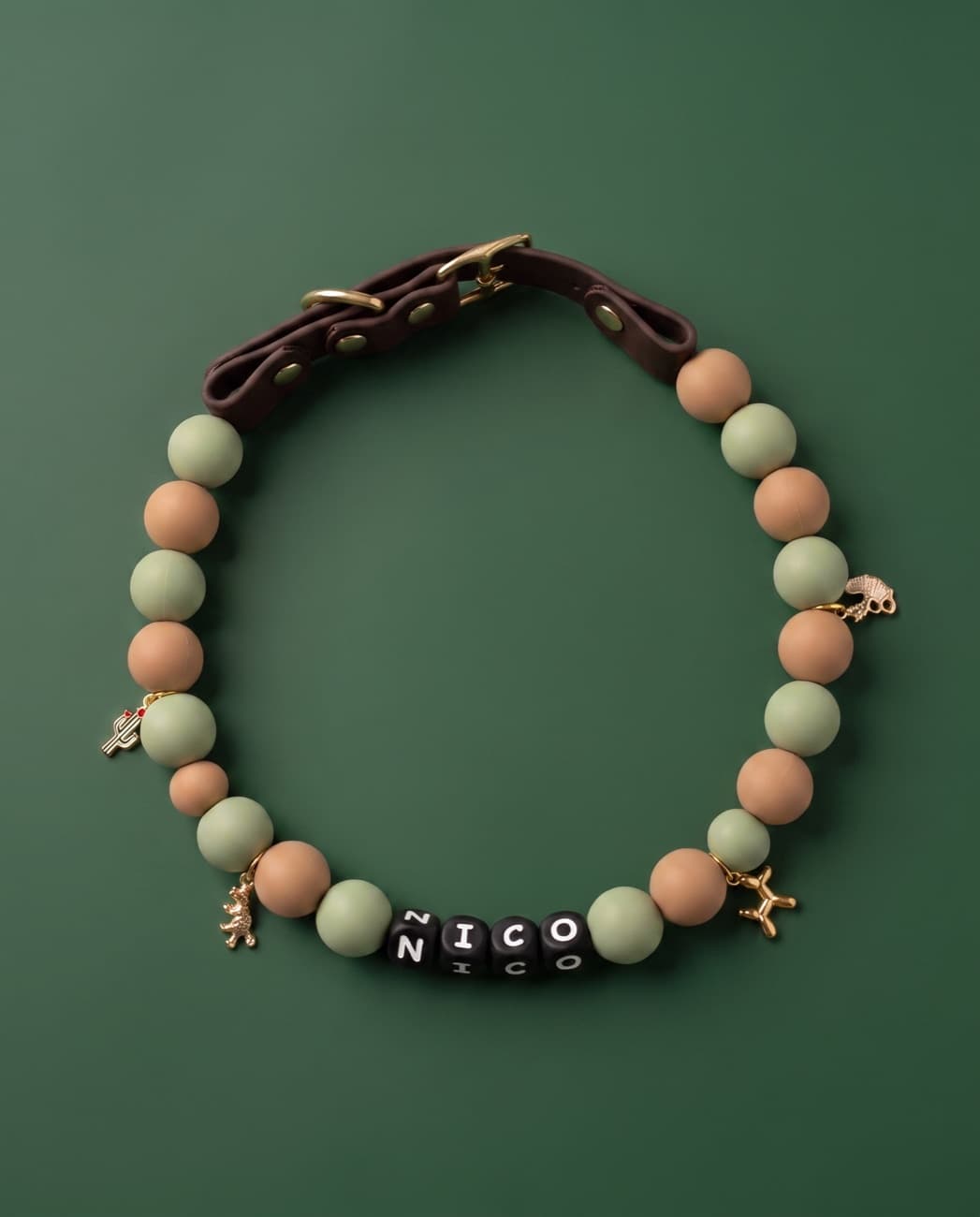Sage-green and warm-sand beaded collar with gold charms on a deep green background